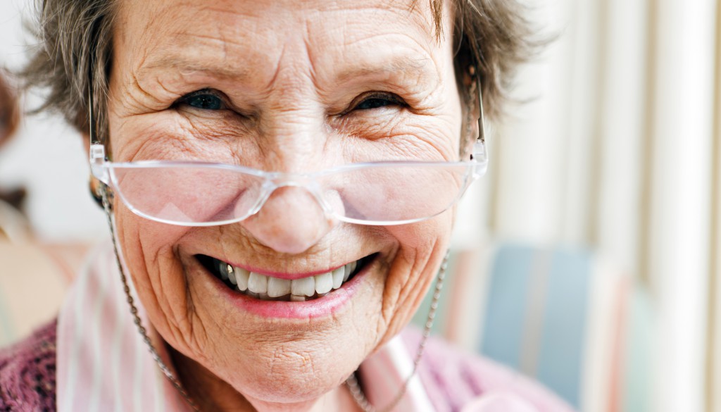 Delighted old woman smiles over her spectacles
